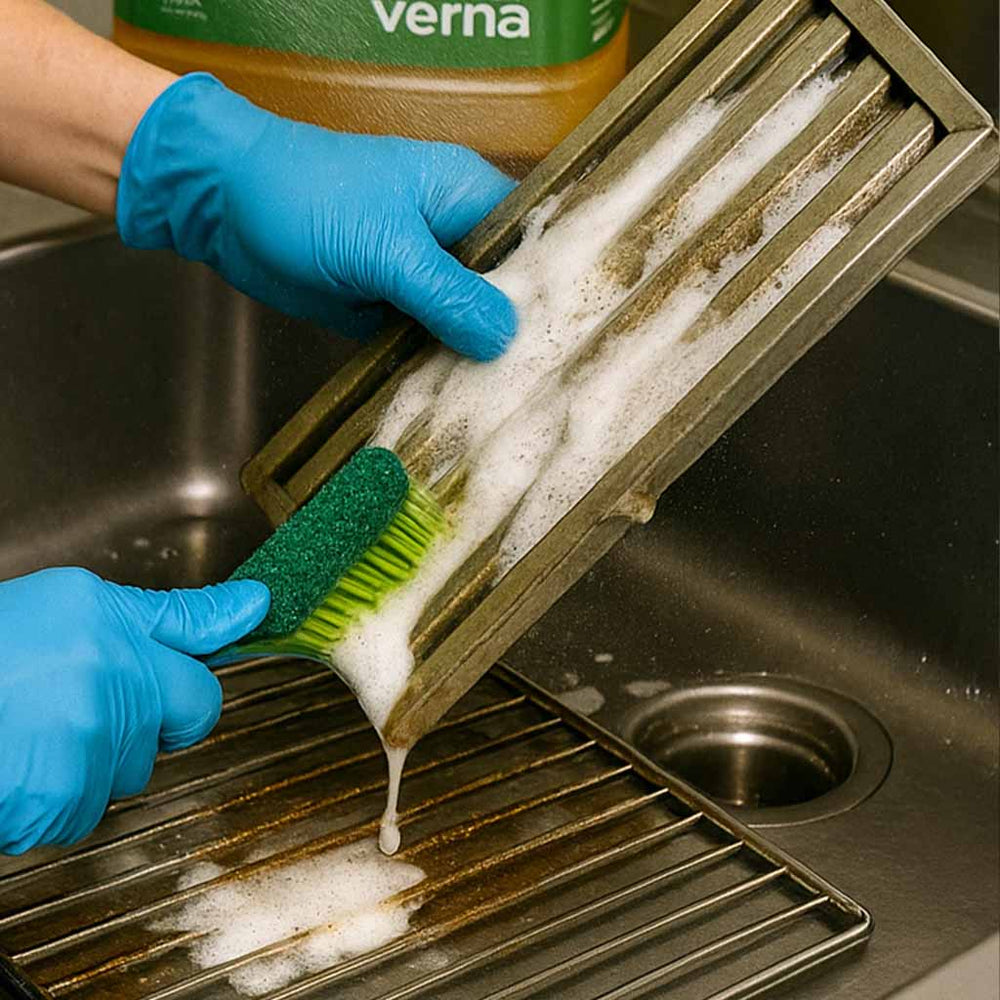 Person cleaning a metal grill with a brush and soap, wearing blue gloves.