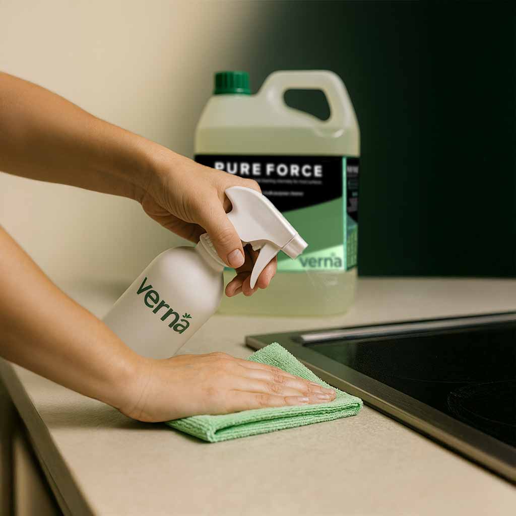 Person cleaning a countertop with a Verna spray bottle and green cloth, with a Pure Force bottle in the background.