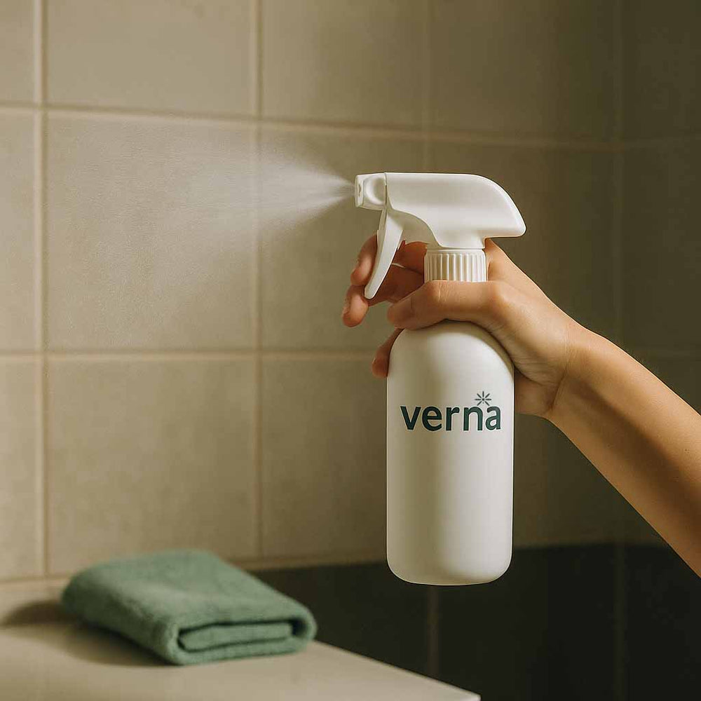 Hand holding a white spray bottle labeled 'verna' against a tiled wall.
